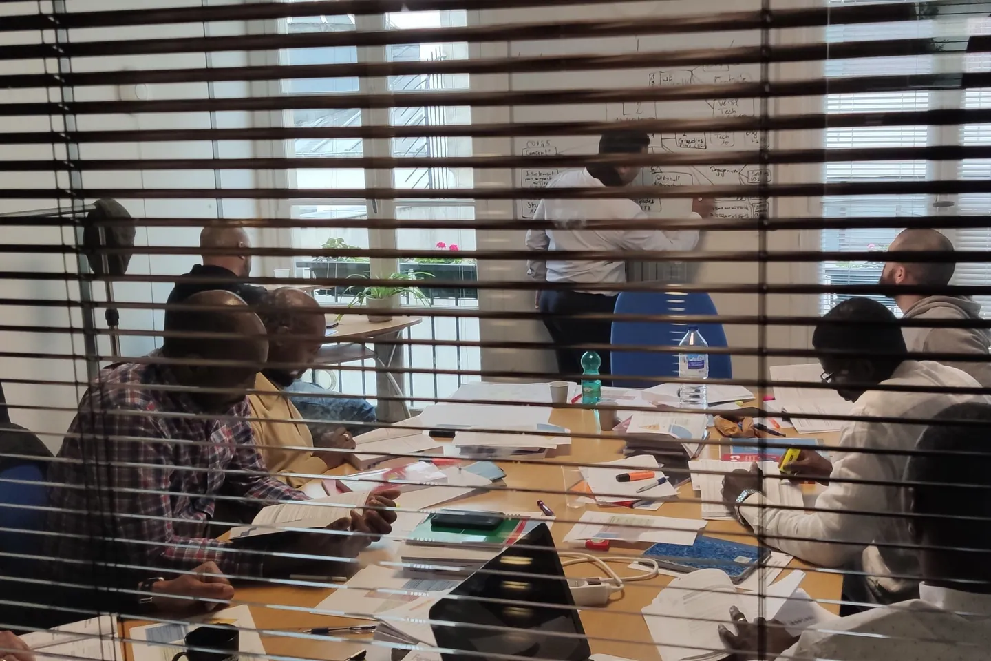 Stagiaires autour d’une table pendant un cours, formateur au tableau blanc