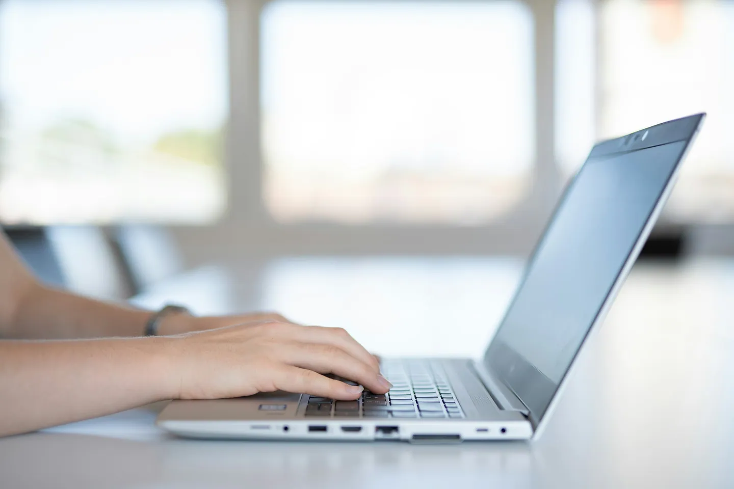 Mains sur le clavier d’un ordinateur portable posé sur une table claire