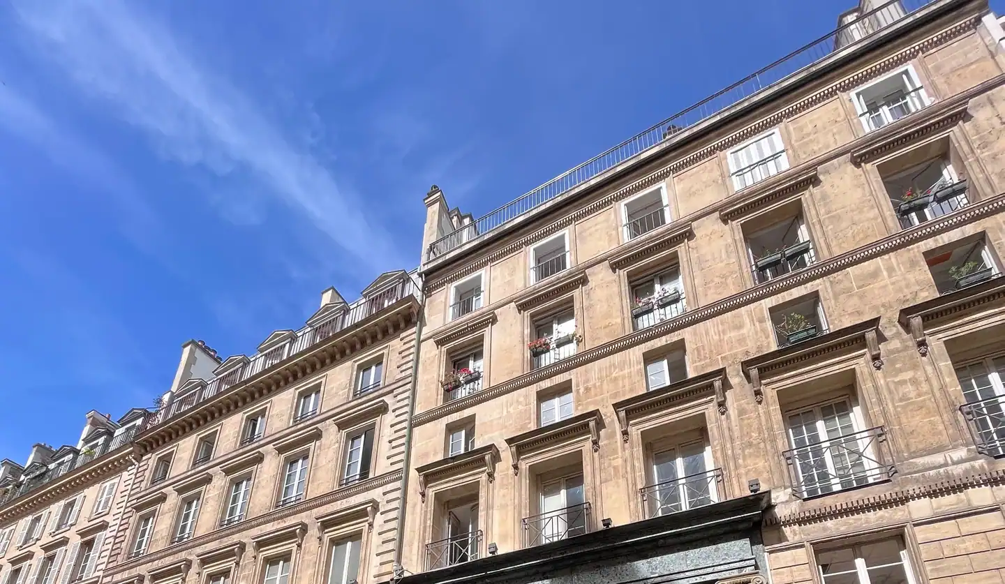 Façade haussmannienne en pierre de taille sous un ciel bleu, typique du quartier de la Bourse